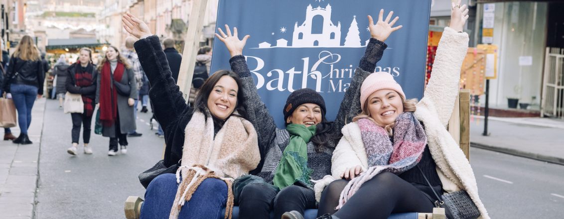 Three women sat on a giant Bath Christmas Market deckchair