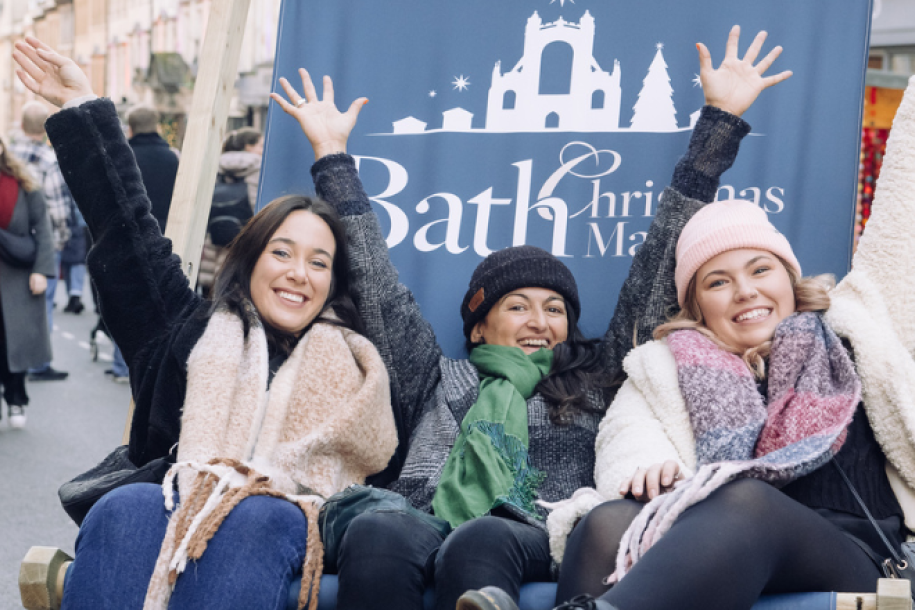 Three women sat on a giant Bath Christmas Market deckchair