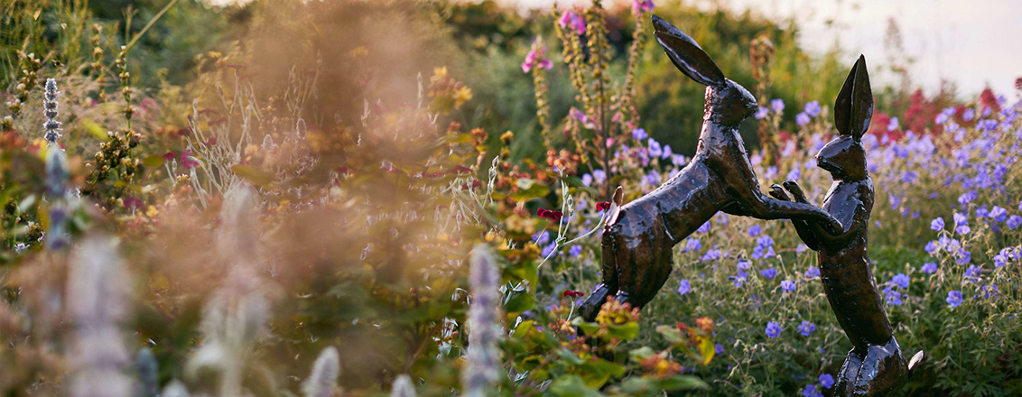 sculpture of two hares in field of flowers